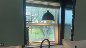 A kitchen with a white sink, dark cabinets, a window with a view of greenery, and a pendant light. - Rustic Ranch Retreat, Farm stay, Firepit, Game Room, Stars (Pauls Valley)