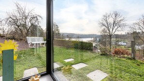 A view through a window of a grassy outdoor area with a bench, trees, and a distant landscape. - Panorama Holiday Home Sorpesee, 120 sqm, Lake View, Private Terrace & Wi-Fi (Sundern)
