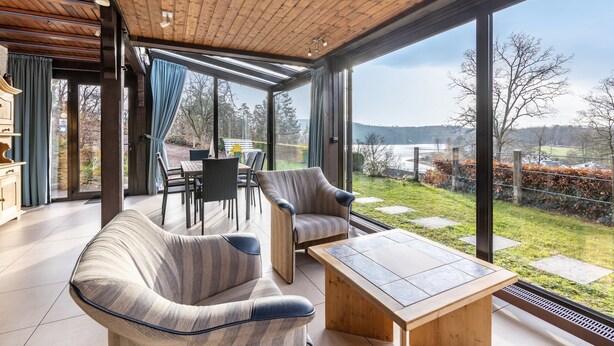 A spacious room with a wooden ceiling, large windows, a sofa, a table, and a view of the outdoors. - Panorama Holiday Home Sorpesee, 120 sqm, Lake View, Private Terrace & Wi-Fi (Sundern)