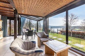 Una habitación amplia con techo de madera, ventanas grandes, un sofá, una mesa y vistas al exterior.