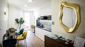 A modern kitchen with a built-in microwave, a sink, and a countertop with a plant. There is a dining area with a table and chairs, and a reception desk with informational brochures. - Cozy and spacious suite near Vatican with private bathroom (Room 3) (Roma)