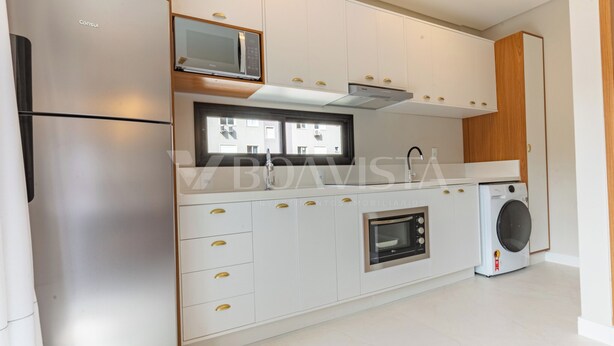 A modern kitchen with white cabinetry, a built-in oven, a microwave, and a washing machine. - Sunny Flats 103 - Piscina Bombinhas (Bombinhas)