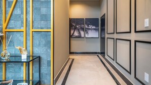 A hallway with a glass table, framed artwork, and a tiled floor. - Sunny Flats 103 - Piscina Bombinhas (Bombinhas)