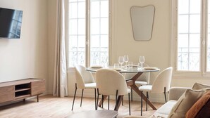 A modern living room with a dining area, large windows, a flat-screen TV, and a minimalist design. - Elegant, fully equipped, air-conditioned accommodation (Le Pré-Saint-Gervais)