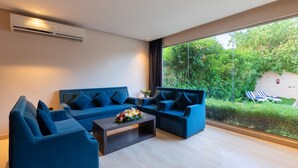 A modern living room with a blue sofa set, a coffee table with flowers, and a large window overlooking a garden. - The Corner Resort (Riyadh)