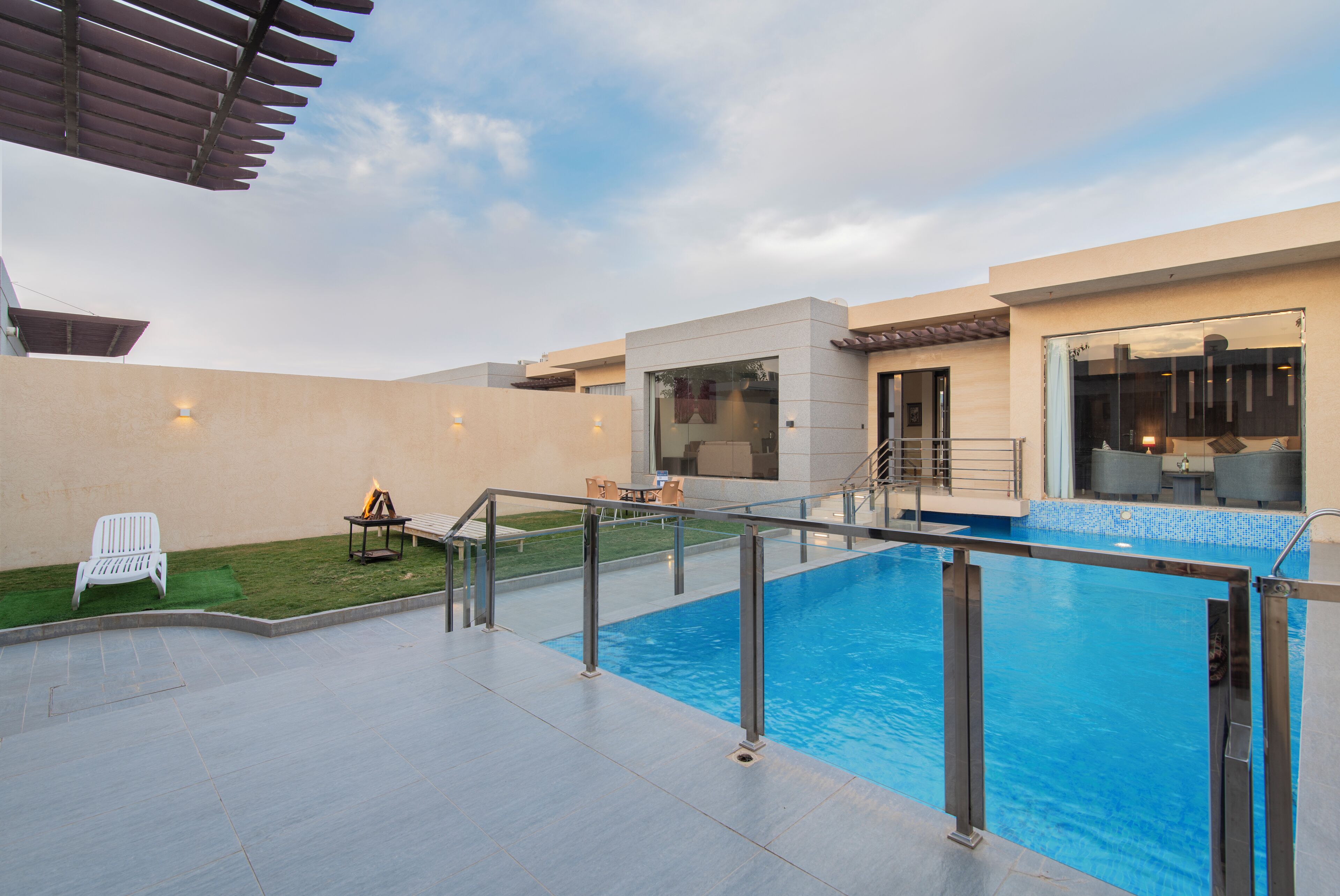 A modern outdoor pool area with a clear sky, a small garden, and a patio with seating.