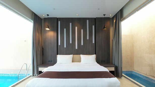 A modern hotel room with a large bed, a view of a swimming pool, and a minimalist decor. - The Corner Resort (Riyadh)