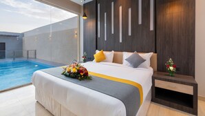 A modern hotel room with a large bed, a bedside table, a nightstand, and a view of an indoor swimming pool. - The Corner Resort (Riyadh)
