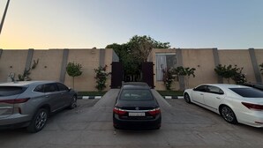 A parking lot with three cars parked in front of a building with a beige wall and a tree. - The Corner Resort (Riyadh)
