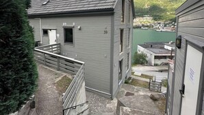A building with a grey exterior, a staircase leading to a door, and a view of a lake and mountains in the background.