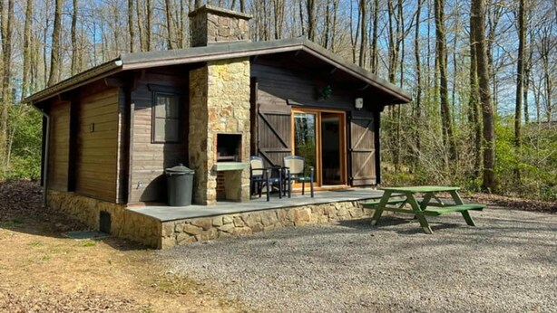 Eine Holzhütte mit einem Steinofen, einer Terrasse mit Tisch und Stühlen sowie einer Steinmauer.