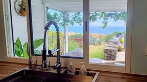Una habitación con área de cocina, un amplio ventanal con vista al mar y una chimenea de piedra.