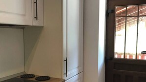 A kitchen with white cabinets, a black stove, and a window with a view of the outside. - Lele Maria's Cottage (Arpașu de Sus)