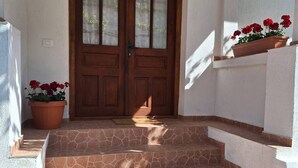 A set of stone steps leading to a wooden door with glass panels, flanked by potted red flowers. - Lele Maria's Cottage (Arpașu de Sus)