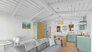 Een moderne keuken met witte kasten, een centraal eiland en een eethoek met een grijze bank en witte stoelen.