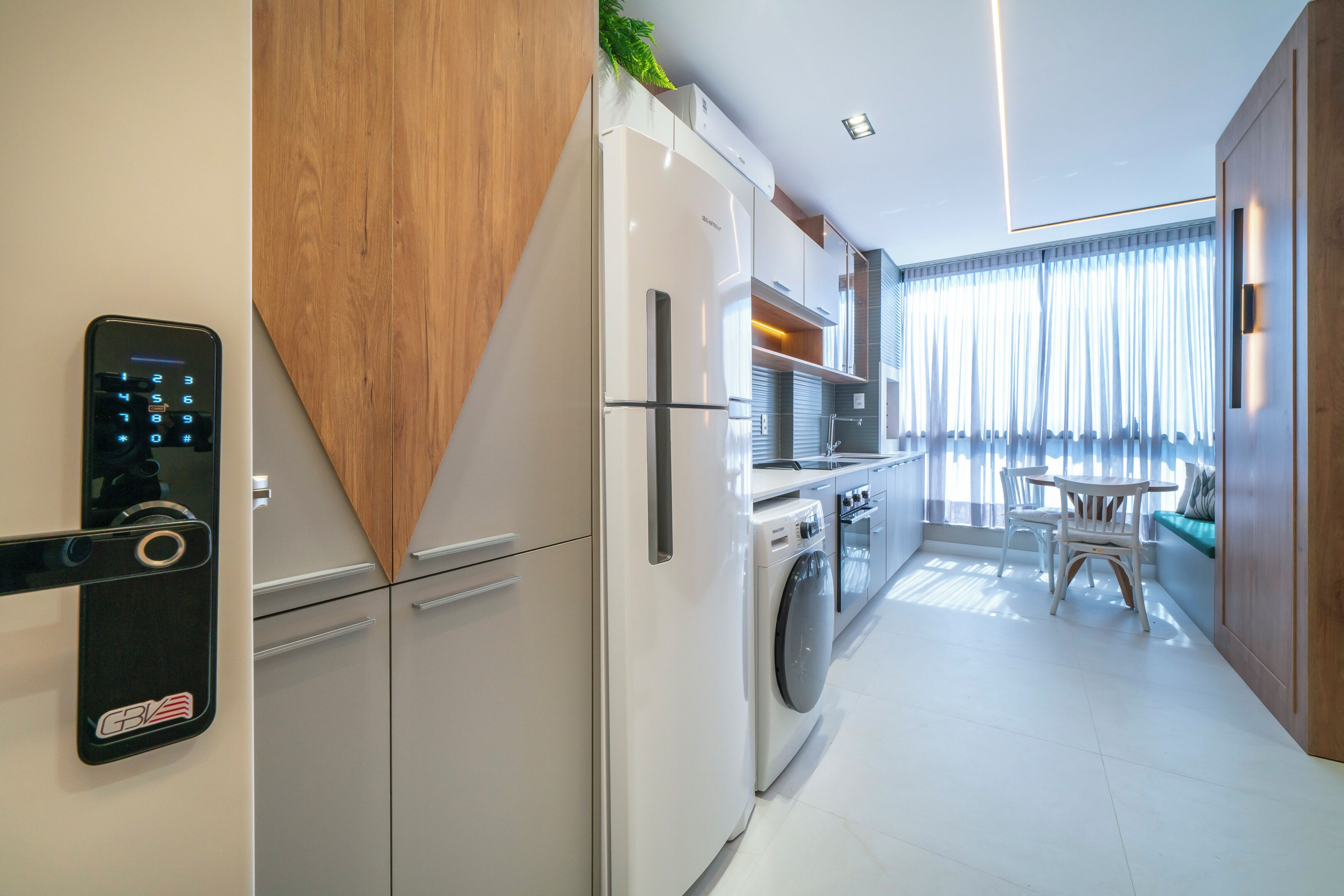 Une cuisine moderne équipée d’un lave-linge encastré, d’un réfrigérateur et d’un panneau de commande fixé au mur.