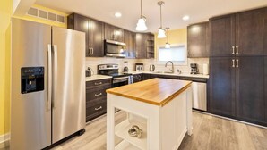 Une cuisine moderne avec des meubles de couleur sombre, des appareils en acier inoxydable, un îlot central en bois et des luminaires suspendus.