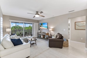 A spacious living room with a ceiling fan, a large TV, and a balcony with a view of the ocean. - 2 bedroom accommodation in Sanibel Island (Sanibel Island)