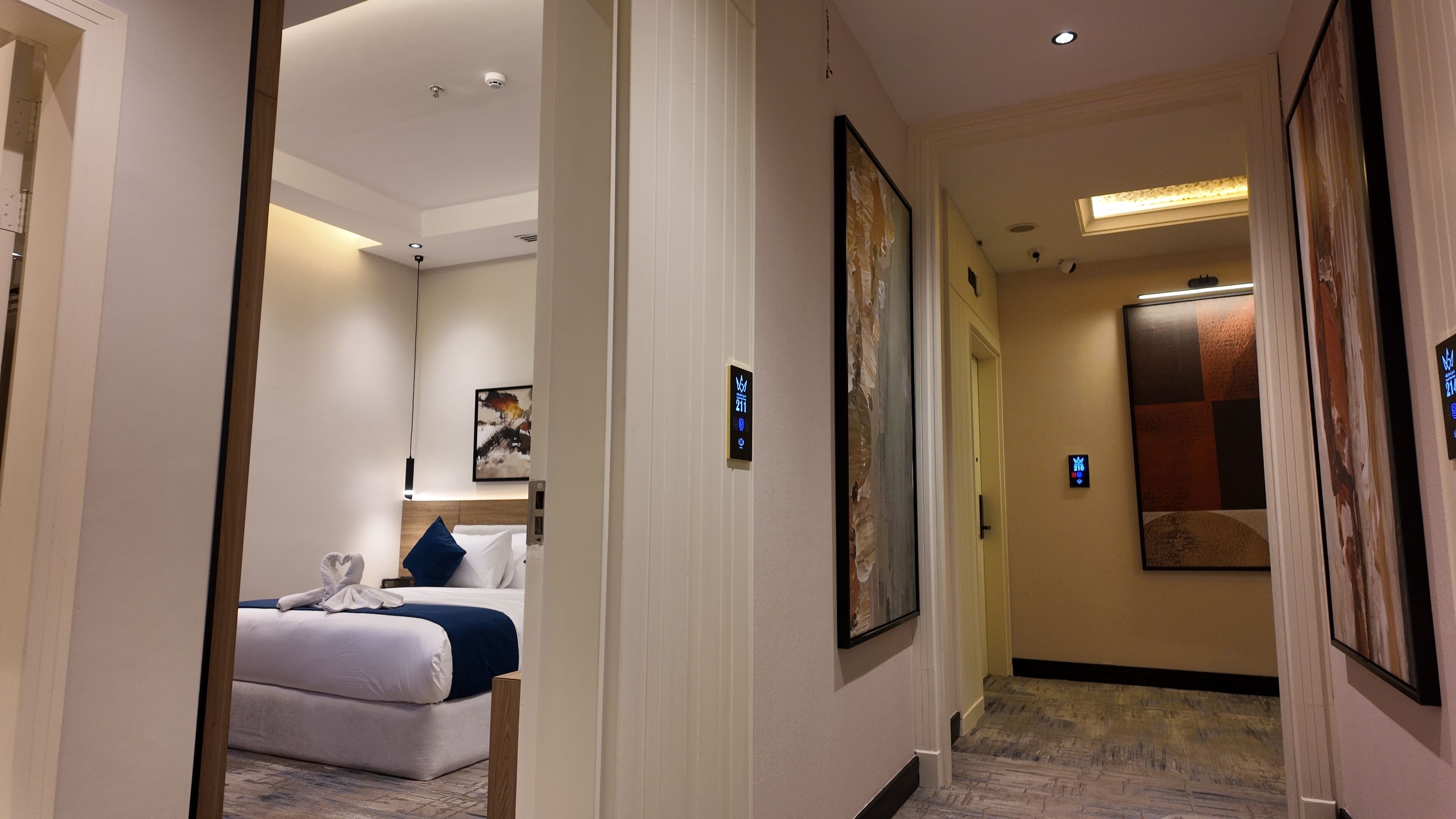 A hotel hallway with a bed, a painting, and a digital sign.