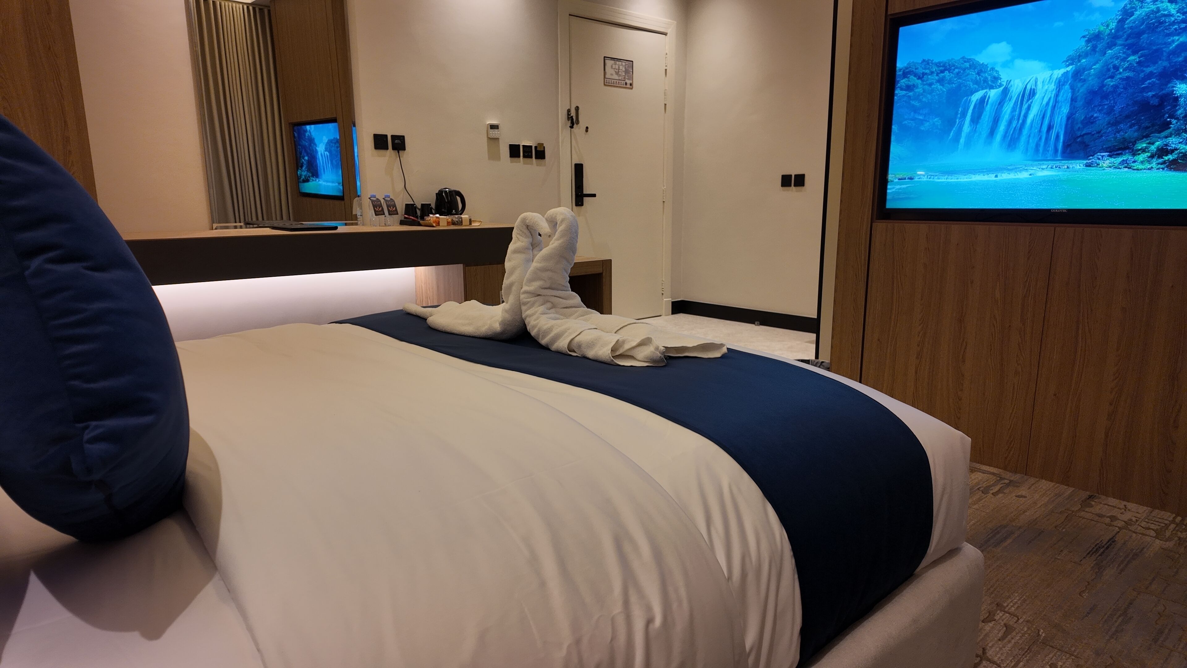 Quarto de hotel com cama, televisão, escrivaninha e máquina de café, além de uma porta.