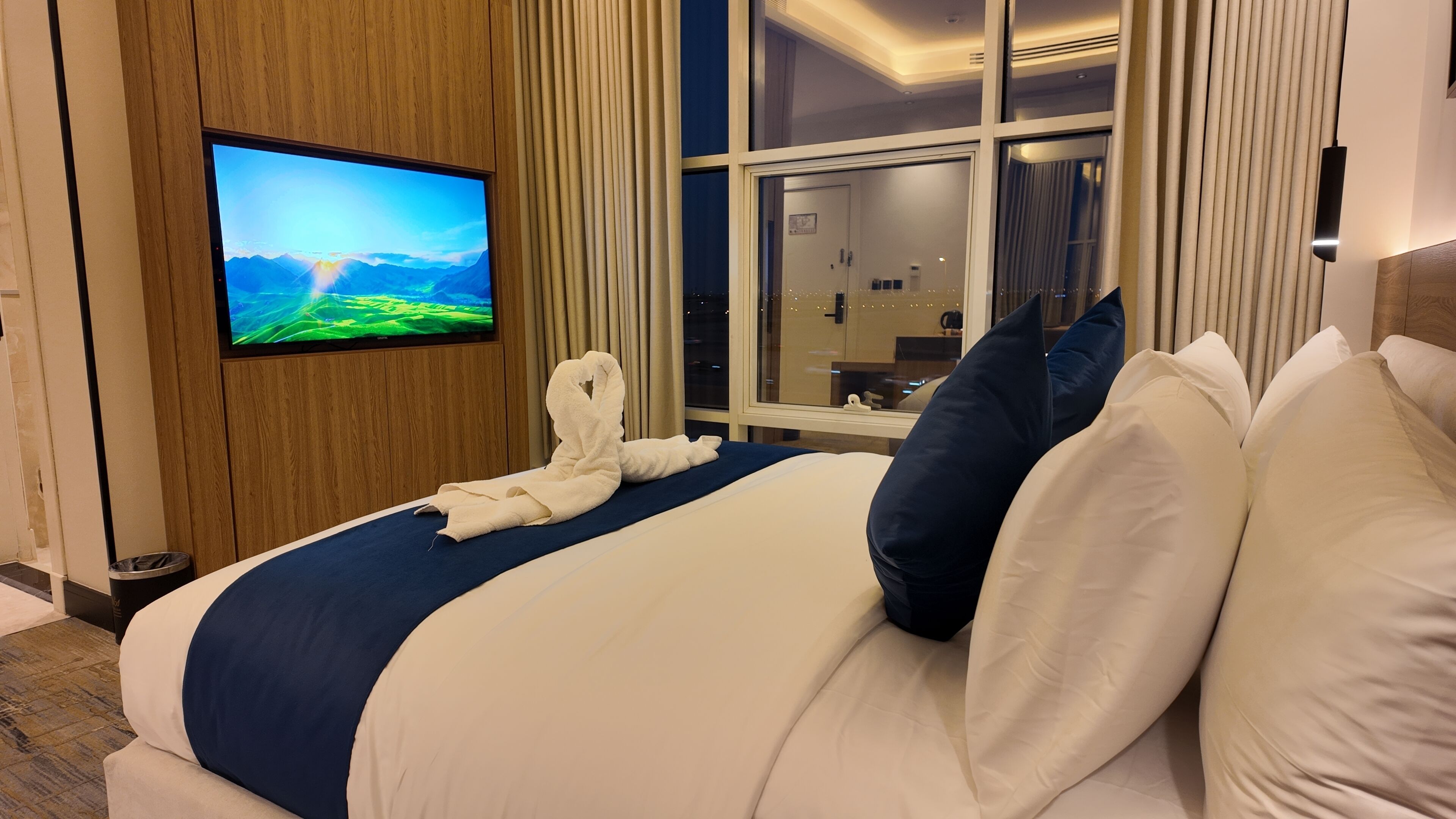 Quarto de hotel com uma cama, televisão na parede e uma janela com cortinas.