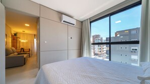 Habitación de hotel con una cama grande, un sofá, un escritorio y vistas a la ciudad a través de amplias ventanas.