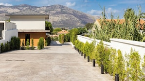 A modern building with a paved courtyard, surrounded by greenery and a mountain backdrop. - Luxury Villa Neptune (Palermo)