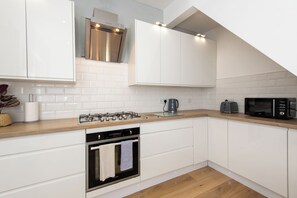 A modern kitchen with white cabinets, a stainless steel range hood, a gas stove, a built-in oven, and a microwave. - Toast Stays - Towngate Terrace (Darlington)