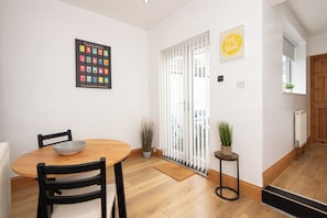 A dining area with a wooden table and chairs, a framed artwork on the wall, and a sliding glass door leading to a balcony. - Toast Stays - Towngate Terrace (Darlington)