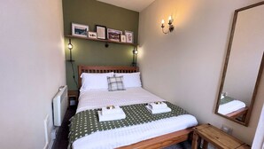 Ein ordentlich bezogenes Bett mit Holz Kopfteil, einem Nachttisch und einem Spiegel an der Wand.