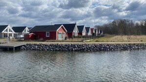 A row of red and white houses by a calm lake with a dock. - Ferienhaus Sanibel mit Kaminofen (Wandlitz)