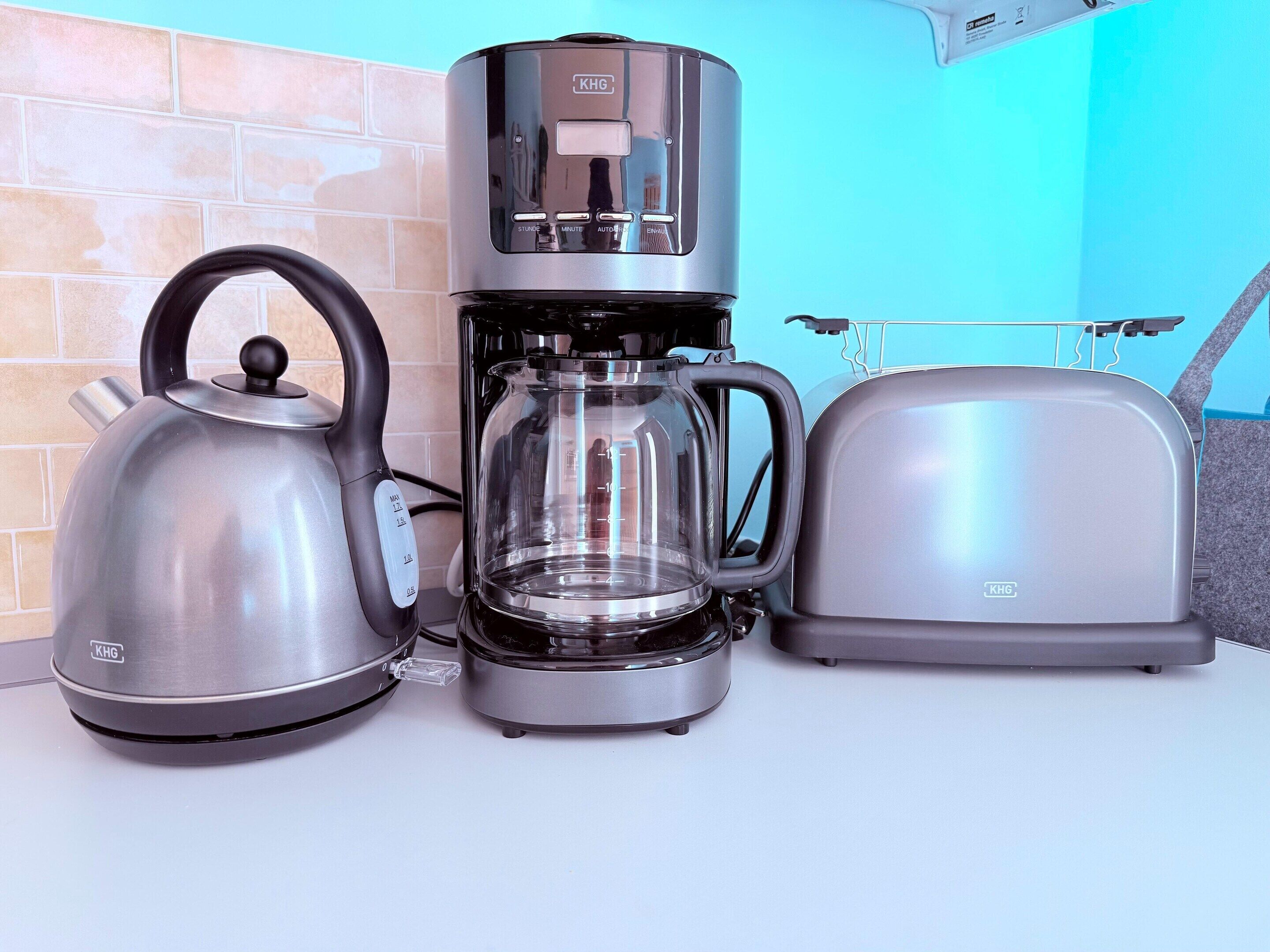 Una tetera de acero inoxidable, una cafetera y un tostador sobre la encimera de la cocina.