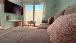 A bedroom with a large bed, a television mounted on the wall, a small round table, and a chair. - Ferienhaus Sanibel mit Kaminofen (Wandlitz)