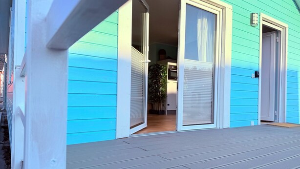 A house with a porch, a sliding glass door, and a small garden visible through the door. - Ferienhaus Sanibel mit Kaminofen (Wandlitz)