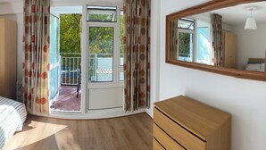 Un dormitorio con una cama, un armario de madera, una mesita de noche con lámpara y un ventanal con cortinas.