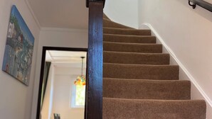 Una escalera con barandilla de madera oscura y peldaños alfombrados en tonos beige que conducen a un comedor con mesa y sillas.