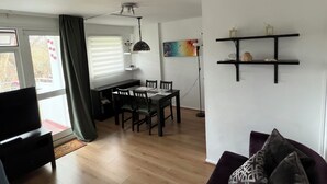 Una sala de estar moderna con comedor, piso de madera, ventilador de techo y televisor.