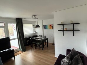 Ein modernes Wohnzimmer mit Essbereich, Holzboden, Deckenventilator und Fernseher.
