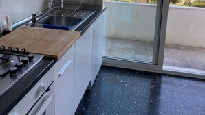 A modern kitchen with a gas stove, sink, and a large window overlooking a balcony with trees. - Penthouse near the beach and bike lane (Sanremo)