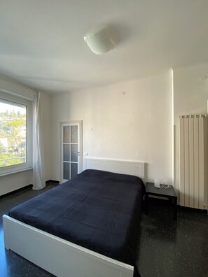 Un dormitorio con cama, un radiador, una ventana con cortinas y una puerta.