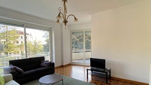 A spacious living room with a large window, a sofa, a coffee table, and a TV on a stand. - Penthouse near the beach and bike lane (Sanremo)