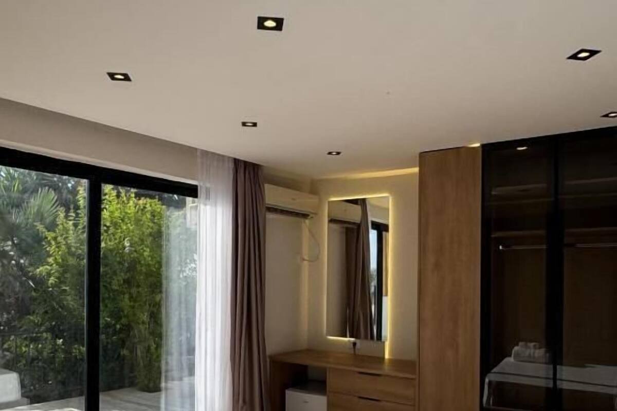Un dormitorio moderno con una cama grande, un tocador de madera, un espejo y un cerramiento de vidrio corredero que da a un espacio exterior.