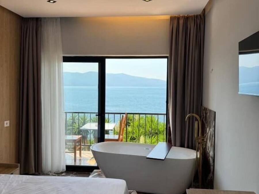 A hotel room with a large bed, a bathtub, and a balcony with a view of the sea.