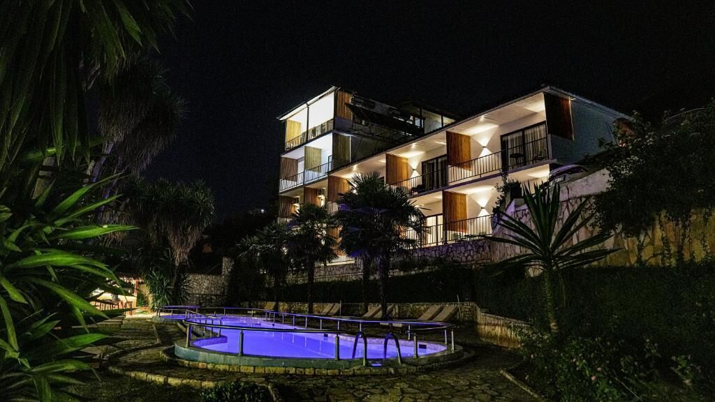 A multi-story hotel with a swimming pool, surrounded by tropical vegetation.