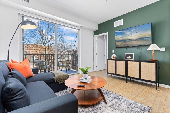 A modern living room with a sofa, coffee table, and a view of the outdoors through large windows. - Cozy 2BR Retreat w/ Gym & Roofdeck near Downtown (Minneapolis)
