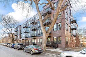 A multi-story residential building with a brick facade, multiple balconies, and parked cars along the street. - Cozy 2BR Retreat w/ Gym & Roofdeck near Downtown (Minneapolis)