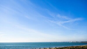 A coastal view with a clear sky, a sandy beach, and a distant shoreline with buildings. - Apartment in Grau-du-roi With Beach Access (Le Grau-Du-Roi)