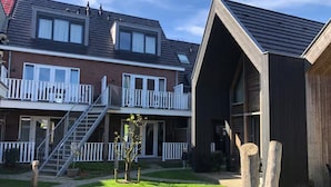Ein Wohngebäude mit einem zweistöckigen Balkon, einer Holzhütte mit geneigtem Dach und einem gepflegten Rasen mit einem Hund.