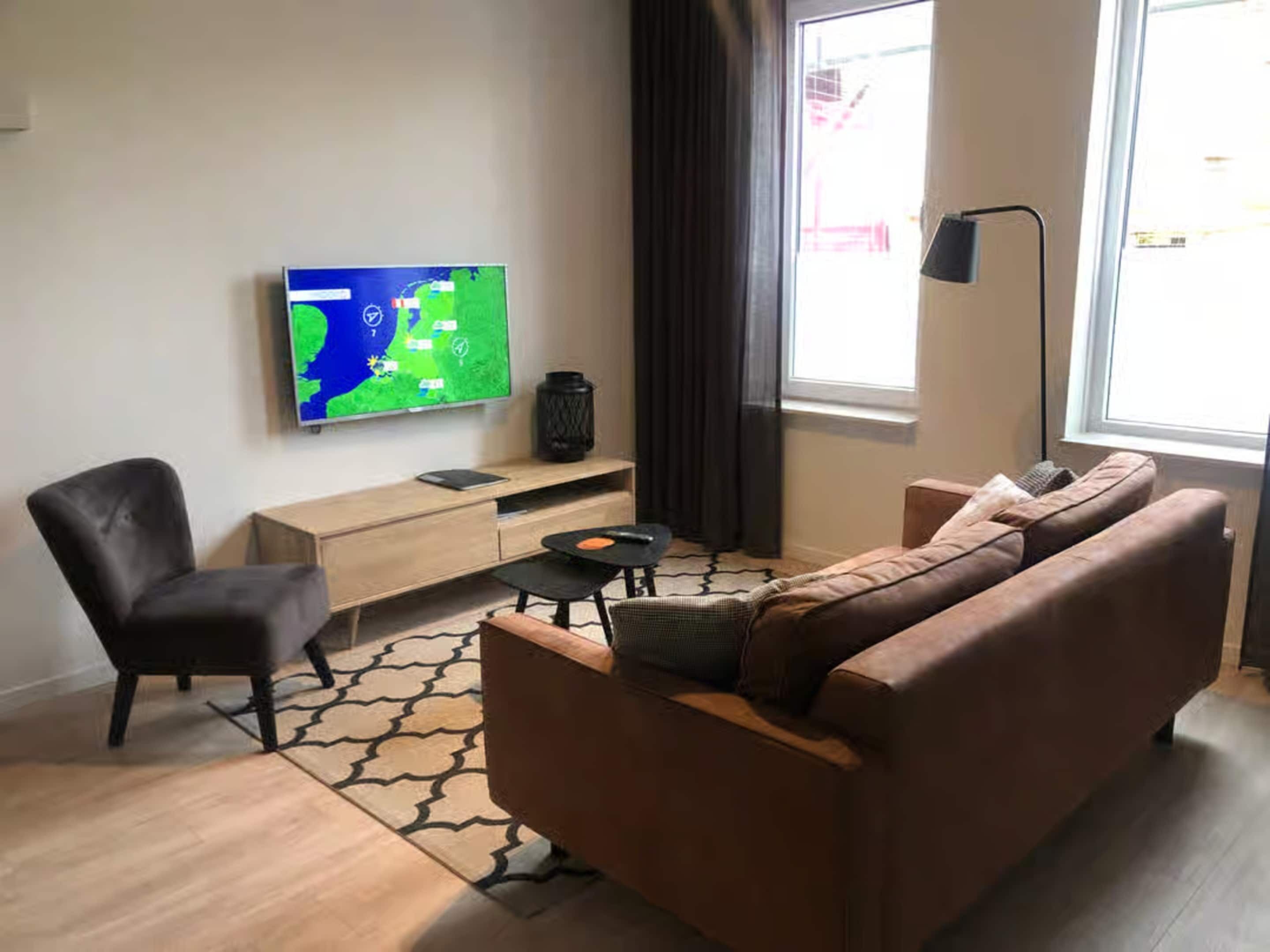 Un salon moderne avec un canapé marron, un fauteuil noir, une petite table et un téléviseur affichant une carte.