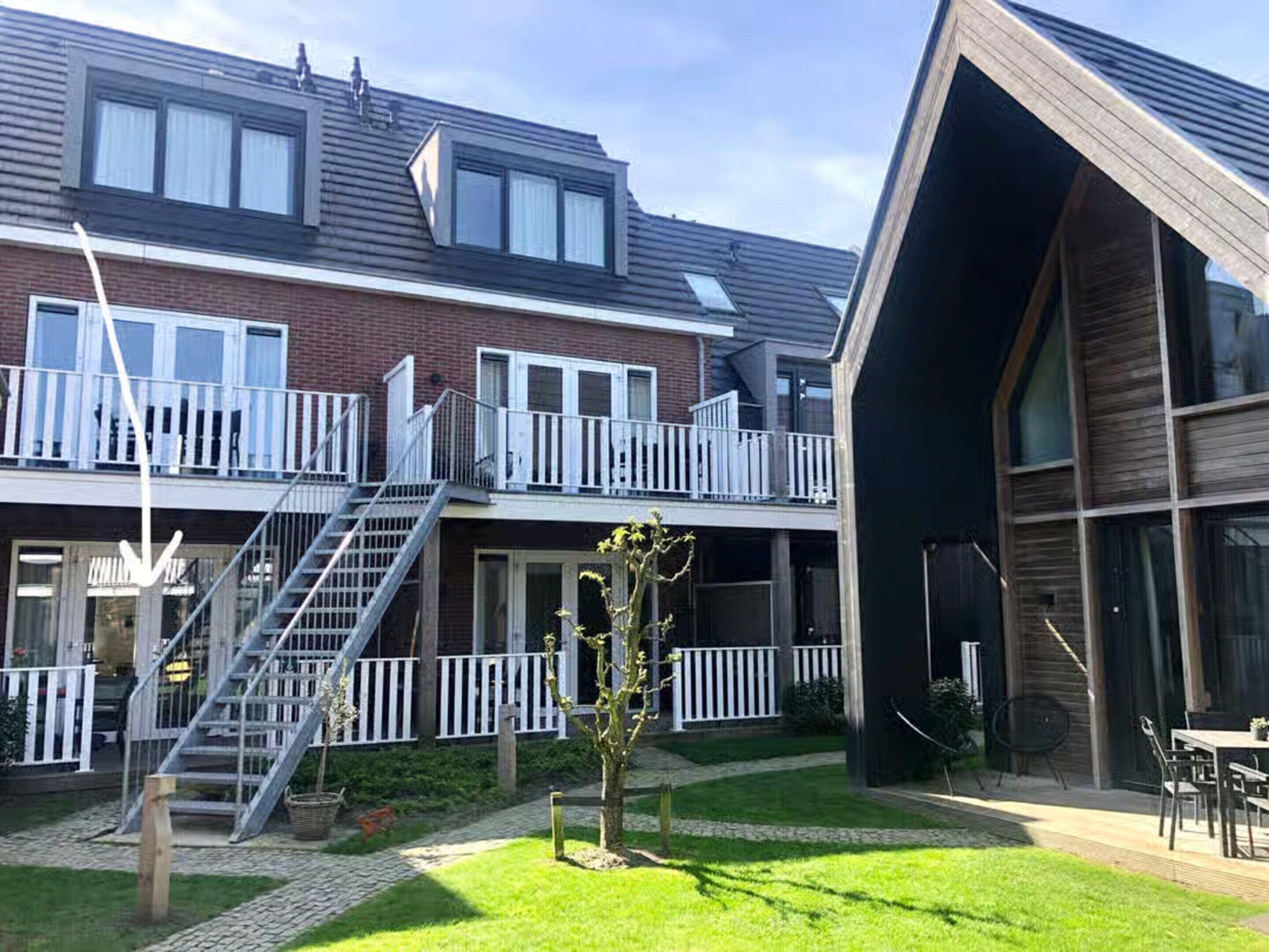En bostadsbyggnad med en tvåvåningsstruktur, en trappa som leder upp till en balkong och en liten trädgårdsyta.